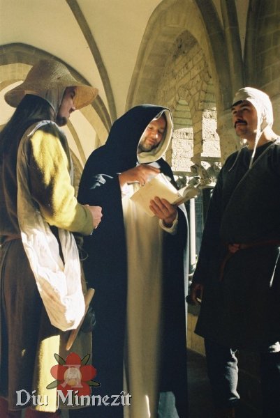 Szene in einem hochmittelalterlichen Kreuzgang: ein Mnch zitiert aus einem Buch. Zwei Handwerker lauschen andchtig.